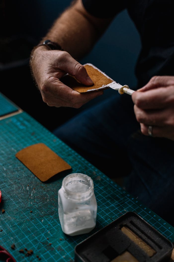 Close-up of hands meticulously crafting leather at a workshop desk.